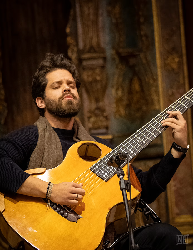 Filipe Moreno sitzt vor einem verzierten Bühnenhintergrund und spielt Bass.
