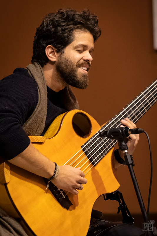 Filipe Moreno lächelt beim Spiel seines sechssaitigen akustischen Basses.