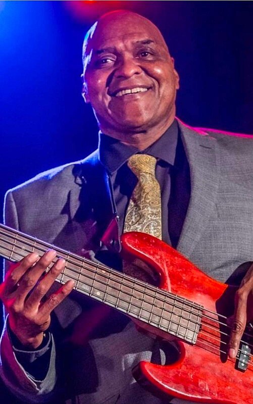 Grant Jones lächelt auf der Bühne und hält einen roten E-Bass.